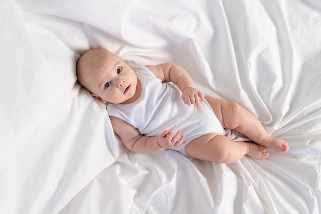 Uma criança em uma cama branca pela manhã. Têxteis e roupa de cama para crianças. Um bebê recém-nascido acordou ou vai para a cama