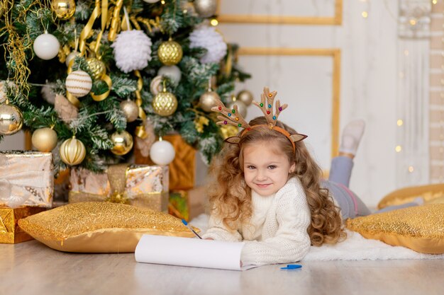 Uma criança escreve uma carta para o Papai Noel sob uma árvore de Natal decorada com ouro