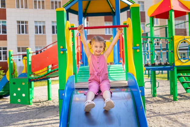 Uma criança feliz brinca no parque infantil do complexo infantil perto de casa no verão no quintal e sorri