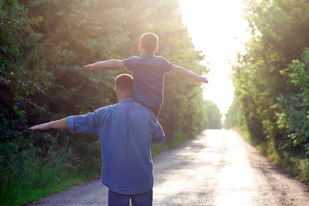 Foto uma criança feliz com um dos pais nos ombros caminha ao longo da estrada no fundo do parque