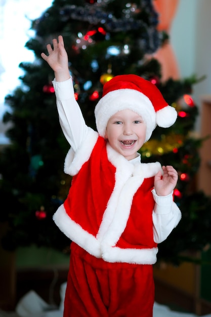 Uma criança feliz em uma fantasia de Papai Noel fica perto da árvore de Natal