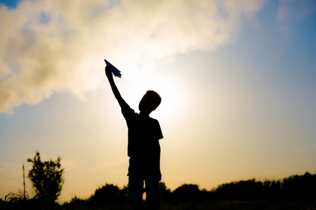 Uma criança feliz está brincando com um avião de papel ao pôr do sol. Aulas com crianças ao ar livre. Estilo de vida