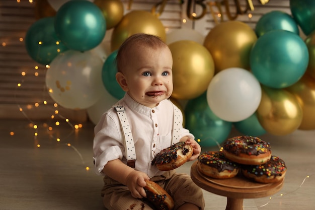 Uma criança feliz no fundo de balões com guirlandas comendo rosquinhas de chocolate