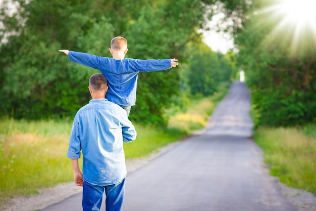 Uma criança feliz nos ombros de um pai na natureza a caminho de viajar