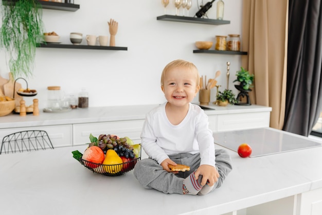 Uma criança feliz sentada na cozinha sorrindo ao lado de frutas e legumes