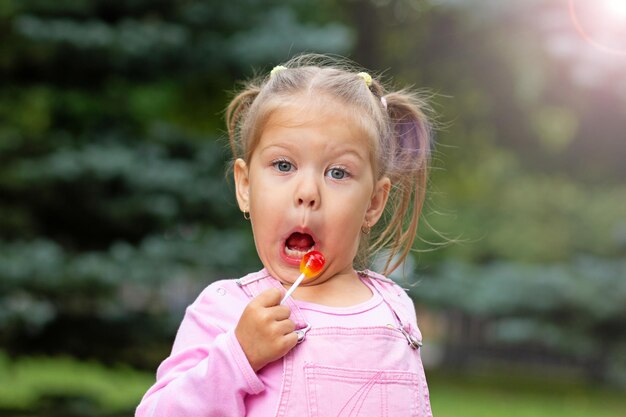Foto uma criança linda com uma cara engraçada a lamber um pirulito.