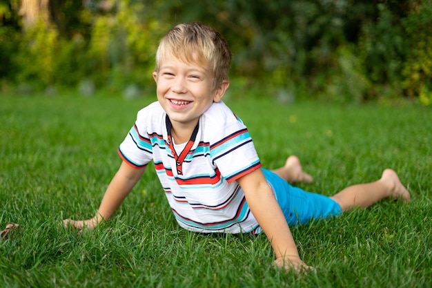 Uma criança loira feliz de olhos azuis deitada na grama sorrindo fazendo exercícios esportes ao ar livre