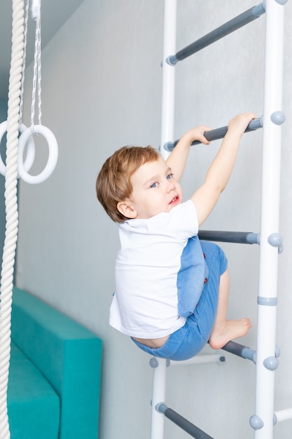 Uma criança na parede sueca pratica esportes em casa, um menino sobe uma escada com uma corda, o conceito de esporte e saúde