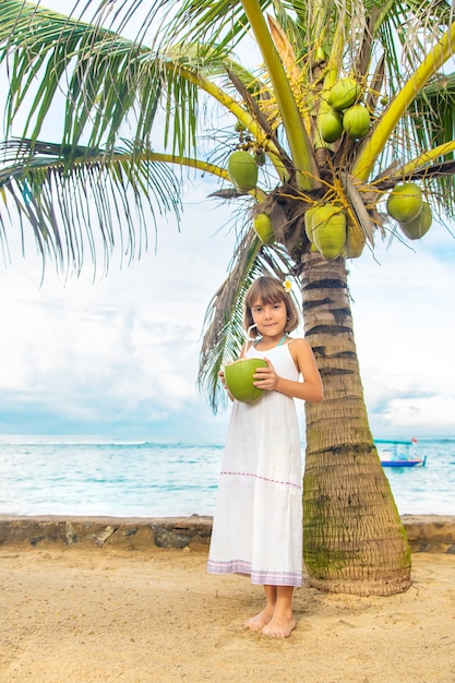 Uma criança na praia bebe coco.