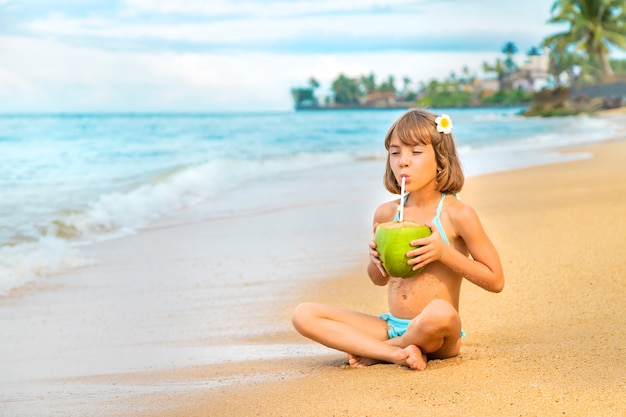 Uma criança na praia bebe coco.