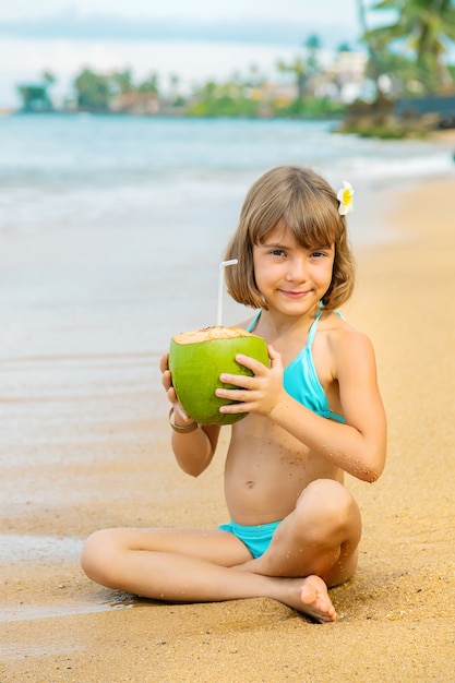 Uma criança na praia bebe coco.