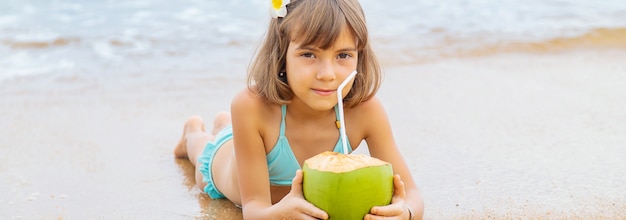 Uma criança na praia bebe coco