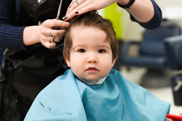 Uma criança no cabeleireiro. O primeiro corte de cabelo da criança no cabeleireiro. Criança de bebê corte de cabelo.