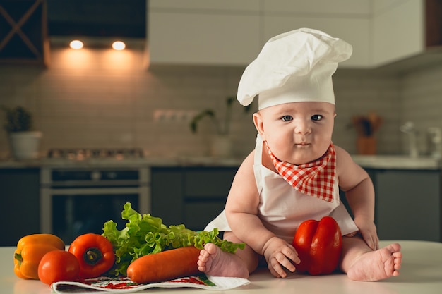 Uma criança no chapéu de um chef senta-se ao lado de legumes