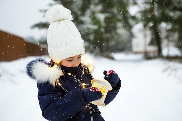 Uma criança no inverno em uma rua com neve sob uma queda de neve em uma guirlanda brilhante com estrelas. Preparação para o feriado de Natal, Ano Novo. Clima festivo, expectativa de um milagre