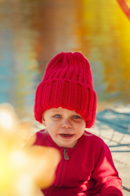 Uma criança no outono no parque chora em um casaco e um chapéu vermelho quente.