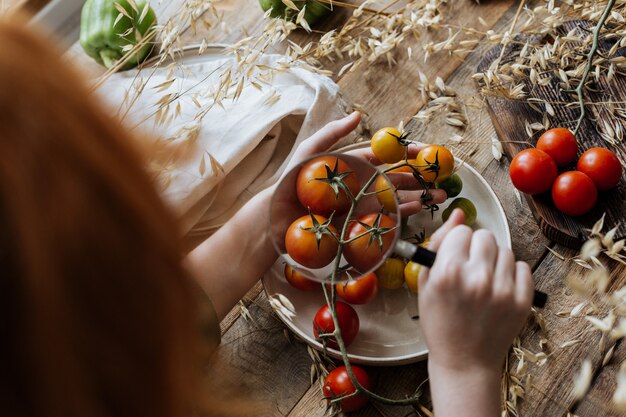 Uma criança olha para pequenos tomates em um galho com uma lupa.