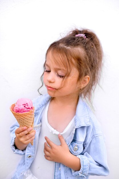 Uma criança olha para uma bola de sorvete rosa em um cone de waffle