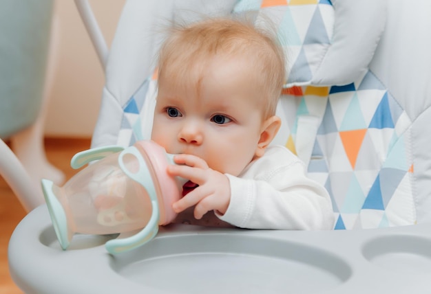 Uma criança pequena bebe água de uma garrafa em uma cadeira alta bebê bebendo de uma garrafa