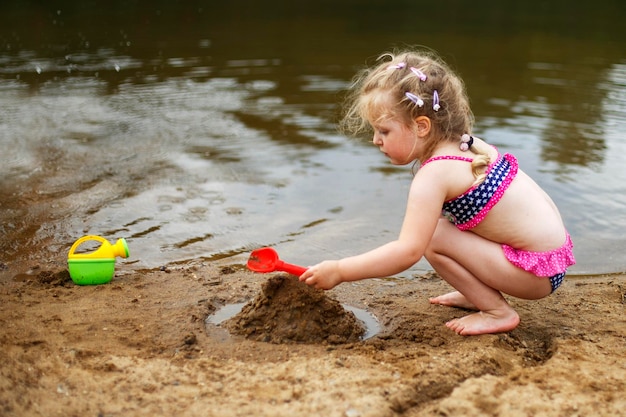 Uma criança pequena brinca com a areia Linda garota sentada na praia