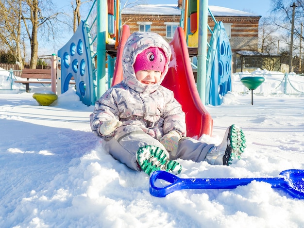 Uma criança pequena brinca no playground com neve.