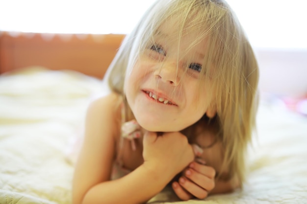 Uma criança pequena com cabelo loiro está na cama a menina está brincando no sofá