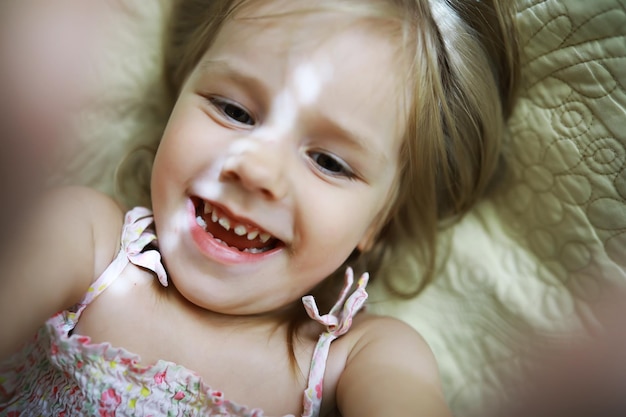 Uma criança pequena com cabelo loiro está na cama A menina está brincando no sofá