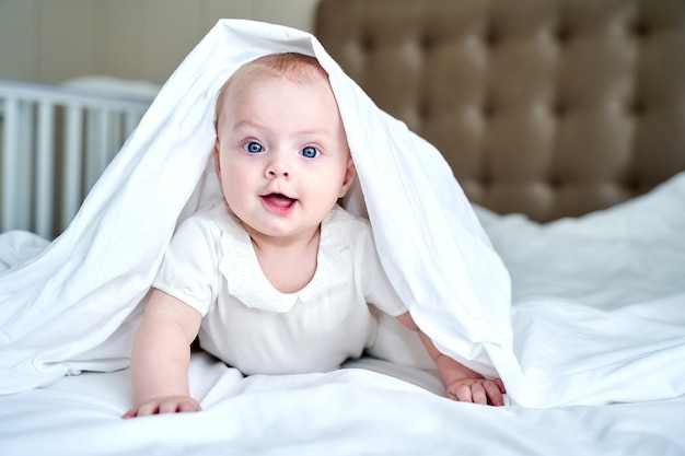 Uma criança pequena com olhos azuis deitada em uma cama branca