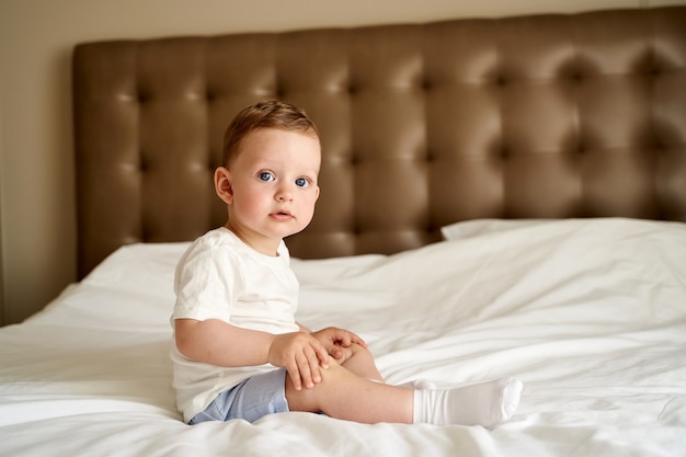 Foto uma criança pequena com olhos azuis sentada na cama