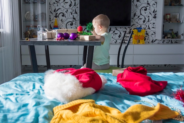 Uma criança pequena com presentes de Natal está sentada em uma mesa de madeira de Ano Novo com um tablet nas mãos