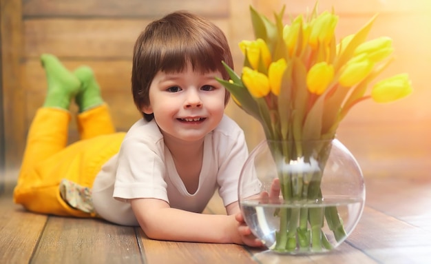 Uma criança pequena com um buquê de tulipas amarelas Um menino com um presente de flores em um vaso Um presente para meninas em um feriado feminino com tulipas amarelas no chão