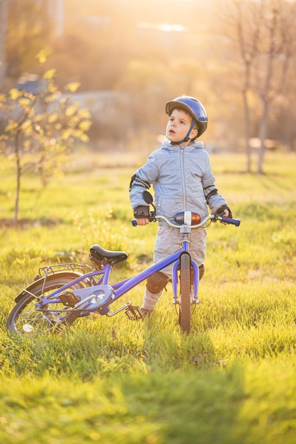 Uma criança pequena com um capacete conduzindo uma bicicleta em um dia ensolarado ao pôr do sol