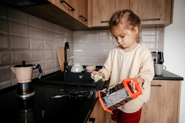 Uma criança pequena com um pano nas mãos fica em uma cadeira perto da pia e lava a louça Uma garotinha ajuda a mãe a cozinhar e limpar na cozinha