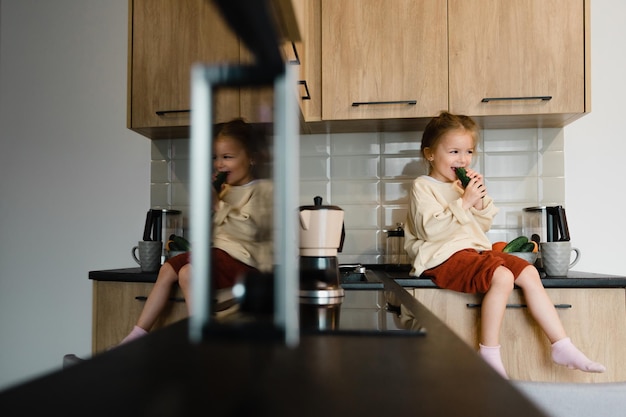 Uma criança pequena com um pano nas mãos fica em uma cadeira perto da pia e lava a louça Uma garotinha ajuda a mãe a cozinhar e limpar na cozinha