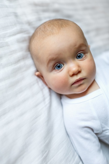 Uma criança pequena de aparência europeia em casa em um fundo claro neutro. uma linda menina bonita olha para a mãe no quadro. retrato de um close-up do bebê recém-nascido.