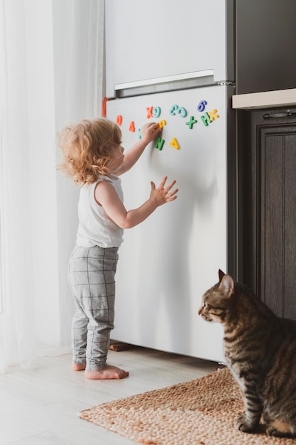 Uma criança pequena e fofa brincando com letras de brinquedo na geladeira