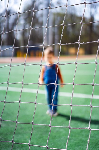 Uma criança pequena está em frente a um gol de futebol A criança está vestindo um macacão azul e uma camisa vermelha