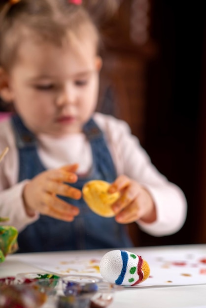 Uma criança pequena pinta ovos com tintas coloridas para a Páscoa