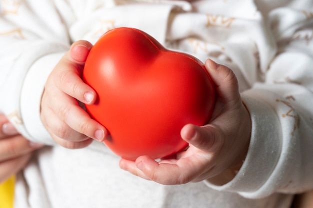 Uma criança pequena tem um coração vermelho nas mãos. conceito de amor materno, saúde infantil