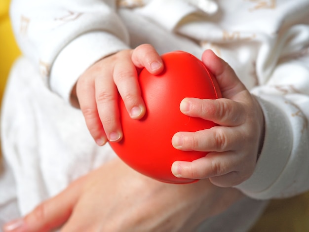 Uma criança pequena tem um coração vermelho nas mãos. Conceito de amor materno, saúde infantil