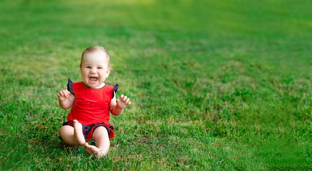 Uma criança rindo no verão na grama verde em um body vermelho nos raios do sol poente se alegra, um lugar de estandarte para o texto