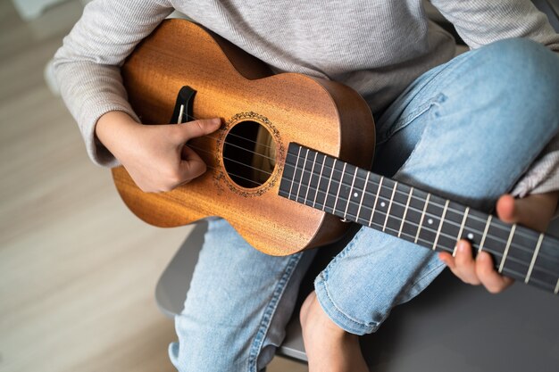 Uma criança tem um ukulele nas mãos. Pequenos filhos criativos. A menina aprende a tocar um instrumento online.