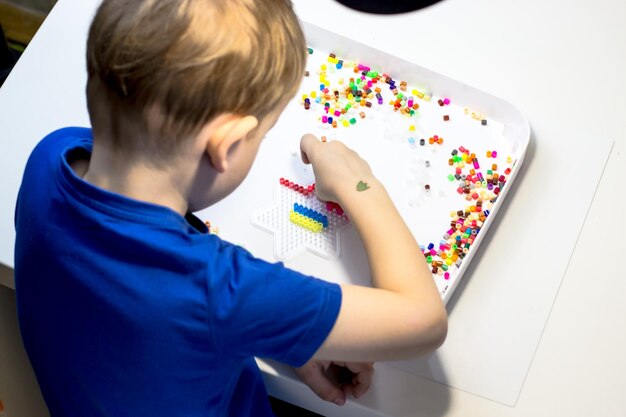 Uma criança toca um mosaico térmico Um menino brincando em uma mesa branca