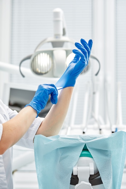 Uma dentista calça luvas num contexto de equipamentos odontológicos em um consultório odontológico.