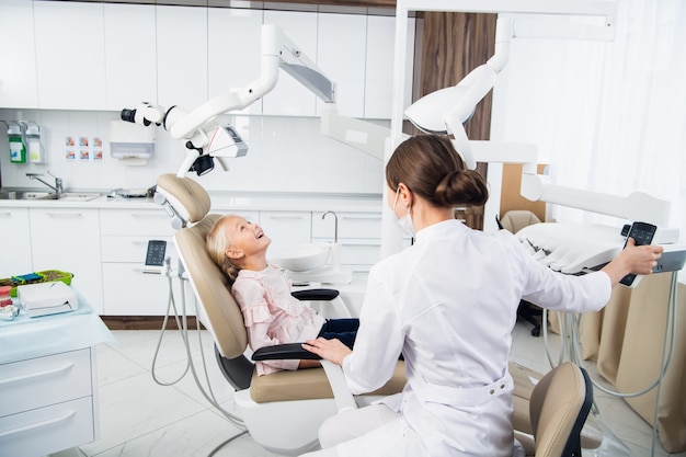 Uma dentista está sentada perto da garota tentando estabelecer um contato com ela para confortá-la antes do check-up.