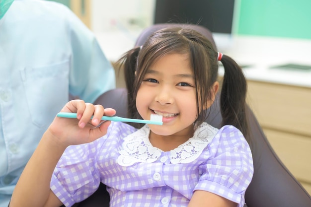 Uma dentista feminina demonstrando como escovar os dentes para uma garotinha na clínica odontológica