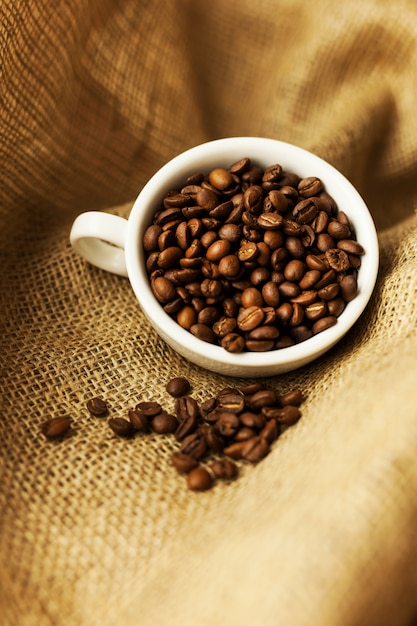 Uma dispersão de grãos de café com uma xícara de café.