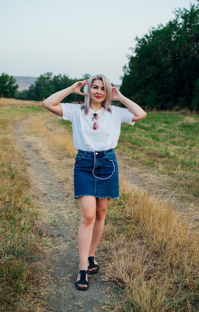 Uma doce jovem feliz alegre mulher bonita caminhando ao ar livre no parque em um lindo dia de verão A menina ouve música com fones de ouvido