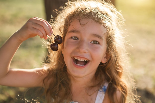 Uma doce menina alegre com bagas de cereja na boca Retrato de verão engraçado de uma criança com presentes de cereja do verão