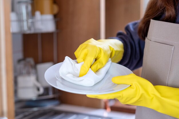 Uma dona de casa usando avental e luva protetora limpando e lavando pratos na cozinha em casa